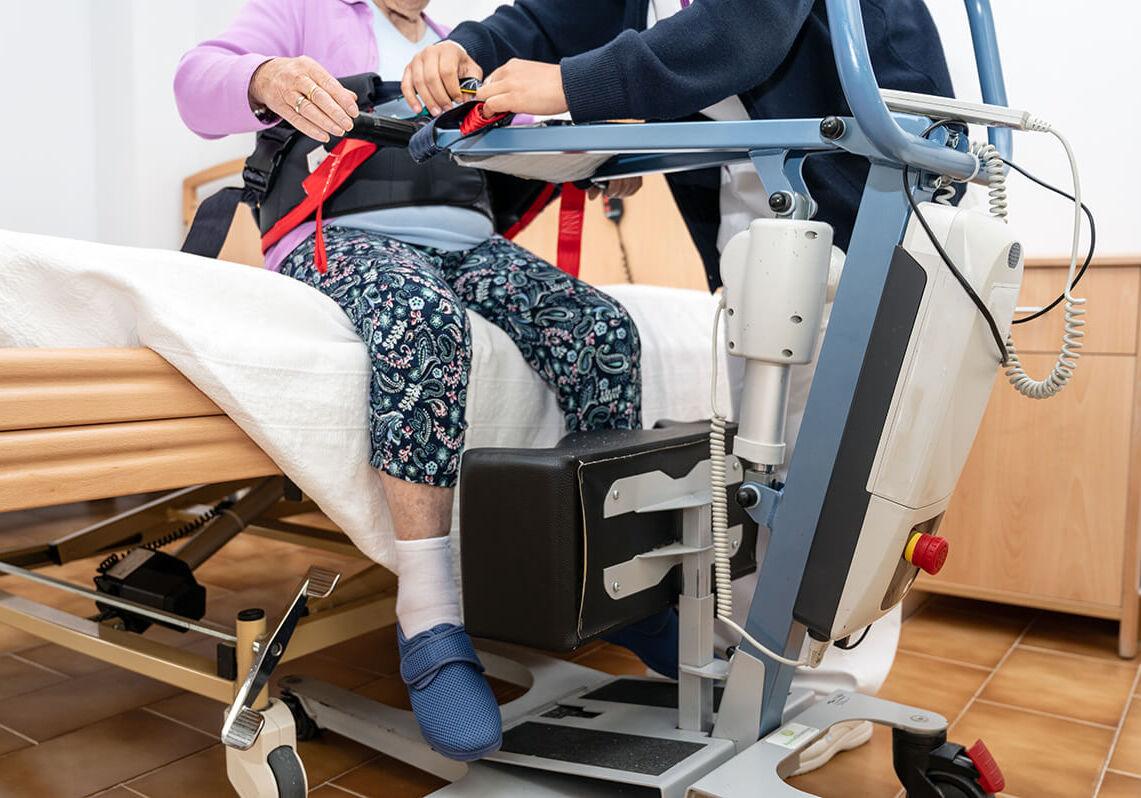 A care staff using a power assist to lifts a patient at nursing home. High quality photography.
